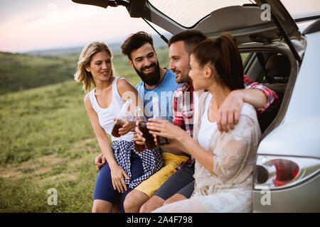 Group of young people sitting in the car trank during trip in the nature Stock Photo