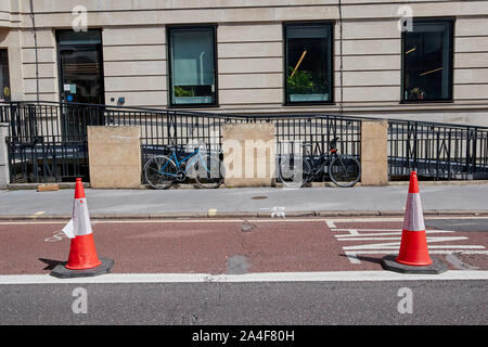 Two bicycles locked up against railings next to traffic cones on a bus lane. Stock Photo