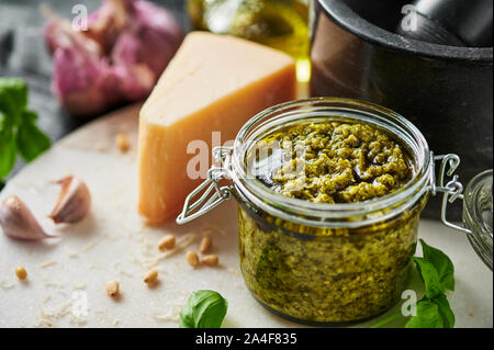 Pesto sauce or pesto genovese in a glass jar with pine nuts, parmesan, basil, oil and garlic on white marble cutting board. Copy space. Stock Photo