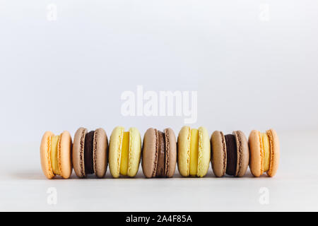 Set of French macarons on a white wooden table. Multicolored macarons. White background, pastel colors. Minimal concept, place for text. Stock Photo
