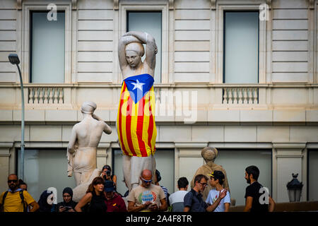 An independence flag is being wrapped around one of the popular sculptures of women in Plaza Catalunya during the demonstration.After knowing the sentence of sedition and embezzlement issued by the Spanish courts with sentences between 9 and 13 years in prison for the leaders of the independence process in Catalonia, thousands of protesters have concentrated on the streets awaiting the first mass action. Stock Photo