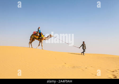 A female tourist on a camel being led by her camel driver across the sand dunes, the Thar Desert, Rajasthan, India. Stock Photo