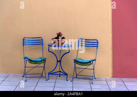 Agios Nikolaus, Crete, Greece. October 2019. Table with two chair and a pot plant on the sidewalk.