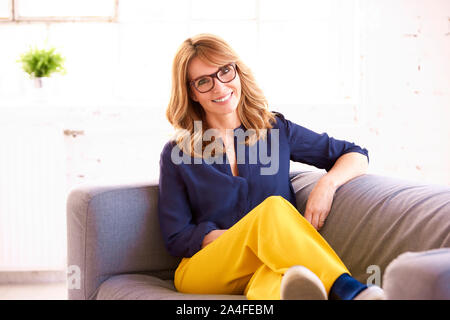 Portrait shot of happy mature woman relaxing on sofa while looking at camera. Stock Photo