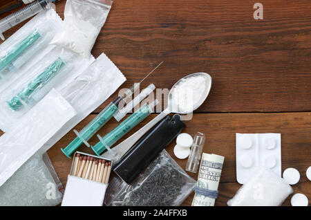 A lot of narcotic substances and devices for the preparation of drugs lie on an old wooden table. Drug dealer stuff. Cocaine and cannabis in complete Stock Photo
