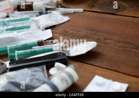 A lot of narcotic substances and devices for the preparation of drugs lie on an old wooden table. Drug dealer stuff. Cocaine and cannabis in complete Stock Photo