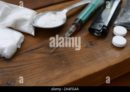 A lot of narcotic substances and devices for the preparation of drugs lie on an old wooden table. Drug dealer stuff. Heroin and methamphetamine in raw Stock Photo