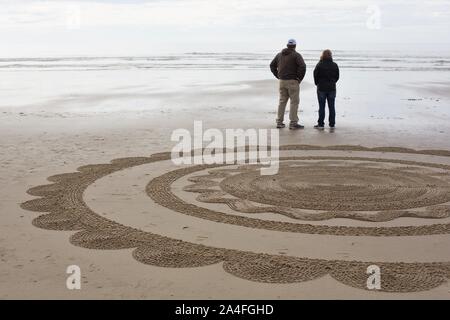 A couple standing next to a section of sand labyrinth by artist Denny Dyke, on Heceta Beach in Florence, Oregon, USA. Stock Photo