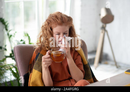Woman taking napkin and drinking tea while having running nose Stock Photo
