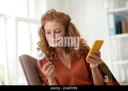 Curly woman holding yellow smartphone after texting doctor Stock Photo