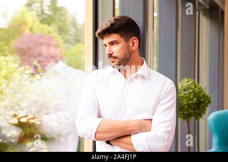 Close-up shot of handsome looking deep in thought while standing at the window and looking out. Stock Photo