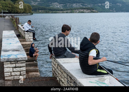 Boys fish on a bank of Lake Pamvotis or Lake Ioannina. Ioannina is the capital and largest city of the Ioannina regional unit and of Epirus, an administrative region in north western Greece. Stock Photo