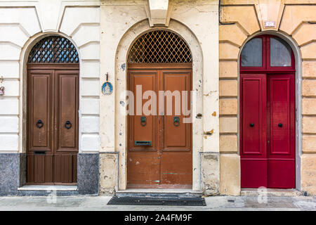 Three old wooden arched doors, brown and red, decorated with iron door knockers and molding. Vintage entry doors in Valletta, Malta. Stock Photo