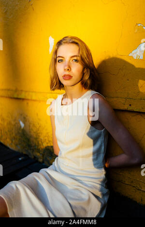 portrait of a woman sitting near a yellow texture wall Stock Photo