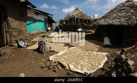 Western Ethiopian Highlands/Ethiopia - April 20, 2019: Grains and pulses set out on mats in a traditional African village with man wrapped in blanket Stock Photo