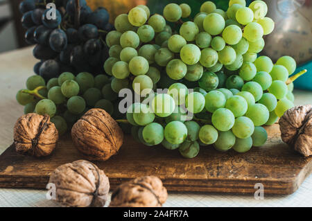 Autumn still life with grapes on a wooden board and walnuts around on a wooden white table. On the back scales. The concept of autumn harvest. Happy Stock Photo