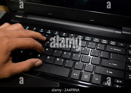 Hacker typing code on laptop keyboard with his fingers Stock Photo