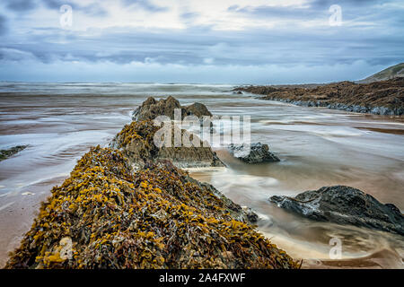 Ebbing tide flowing around exposed rocks Stock Photo