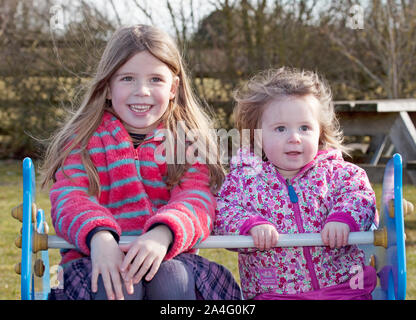 Sisters sat on swing in park, England Stock Photo