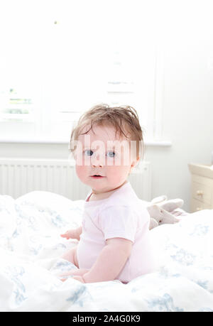Baby sat in bed looking at camera Stock Photo
