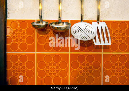 Retro kitchen tools hangs on vintage orange tiled wall background Stock Photo