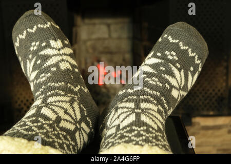 feet in woolen winter socks with white ornament  near fireplace in winter evening, concept of relaxing cozy  New Year night and  Christmas at the home Stock Photo