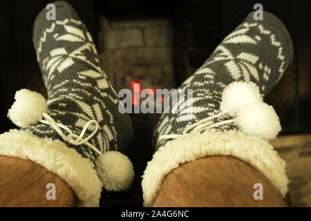 male hairy feet in woolen warm socks with ornament and white pom poms near fireplace in winter evening, concept of relaxing cozy New Year night