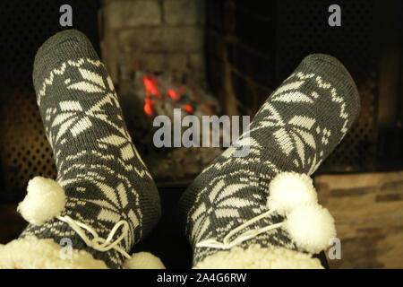 feet in woolen winter warm socks with white ornament and  pom poms near fireplace in winter evening, concept of relaxing cozy New Year celebration