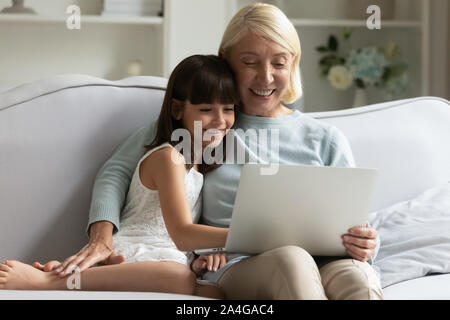 Small girl with granny shopping, watching funny movie on laptop. Stock Photo