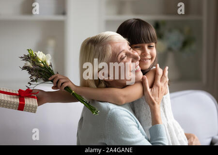 Excited middle aged woman cuddling smiling adorable little granddaughter. Stock Photo