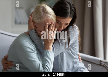 Empathic young lady embracing soothing crying depressed elder mommy. Stock Photo