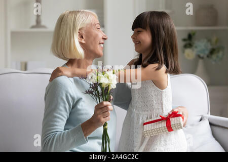 Happy preschool cute girl congratulating smiling middle aged grandmother. Stock Photo