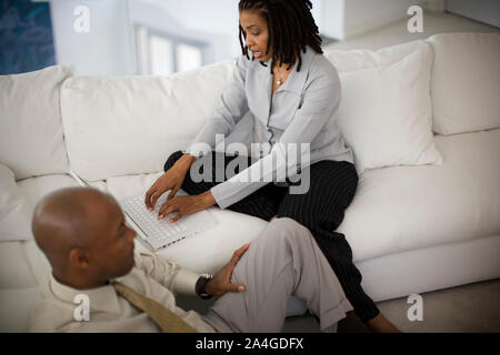 Young woman using a laptop while sitting on a couch next to her husband. Stock Photo