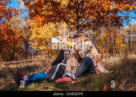 Senior couple taking selfie in autumn park. Happy man and woman enjoying nature and hugging Stock Photo