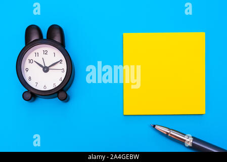 Flat lay of a paper for blank notes and alarm clock to write messages, isolated on blue background. Stock Photo