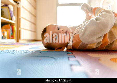 Baby lying on the floor watching the camera with curiosity. Stock Photo