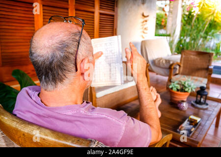 Retired and bald man relaxes sitting in a garden while completing his hobbies. Stock Photo