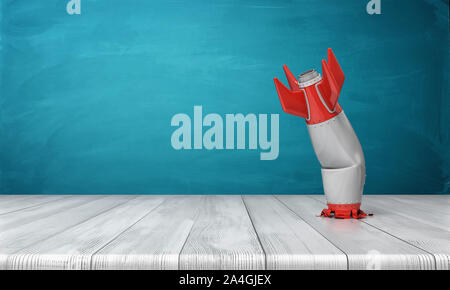 3d rendering of a red and silver realistic model of a retro rocket stands crashed into a wooden desk on a blue background. Stock Photo