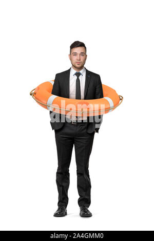 A young businessman stands on a white background while inside an orange life buoy. Stock Photo