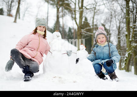 Two adorable young girls having fun together in beautiful winter park. Cute sisters playing in a snow. Winter activities for family with kids. Stock Photo