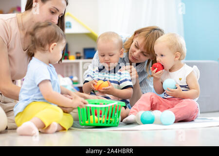 Adorable babies toddlers playing at home or kindergarten, cutting plastic vegetables and tasting these toys. Games in creche Stock Photo