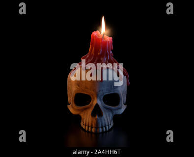 A concept showing a human skull topped with a melting red lit candle on an isolated dark studio background - 3D render Stock Photo