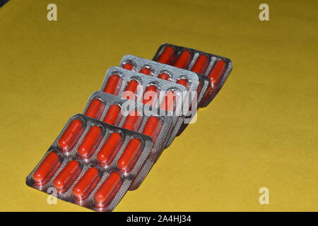 Red pill capsules in blister pack isolated on yellow background, in the strips. Stock Photo