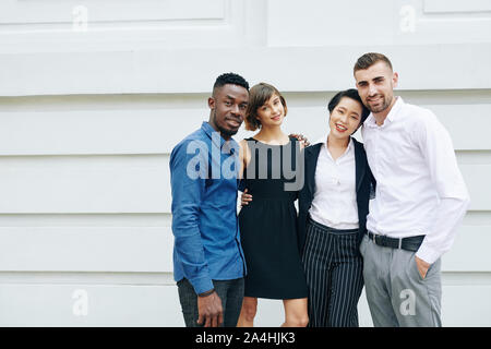 Group of happy hugging young business people standing outside the office building Stock Photo