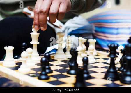 White chess king alone surrounded by the opposite pieces, selective focus on white chess king piece, male hand touching about to move a chess piece Stock Photo