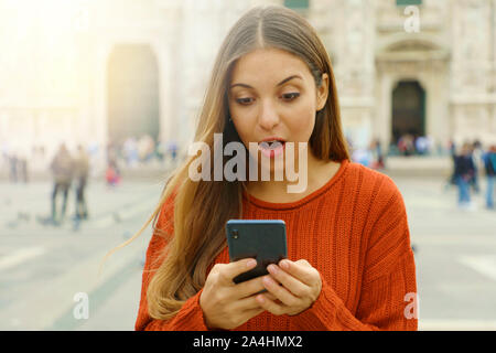 Surprised girl looks at mobile phone in city square in autumn. Stock Photo