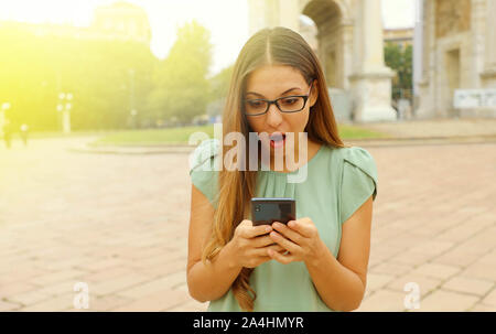 Pretty astonished business woman looks her smart phone in the square. Stock Photo