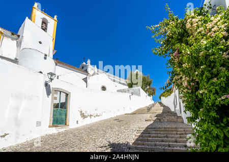 Steep cobbled street in Tavira old town leading to Tavira Castle and St. Mary's Church, Algarve, Portugal Stock Photo
