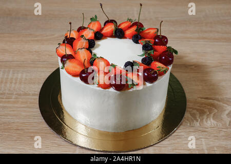 beautiful cake with strawberries, cherry, blackberry and cream on the wooden background. Stock Photo