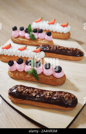 Traditional French dessert. Eclair with cream, chocolate icing, strawberries, cherry, mint on wooden background close up Stock Photo